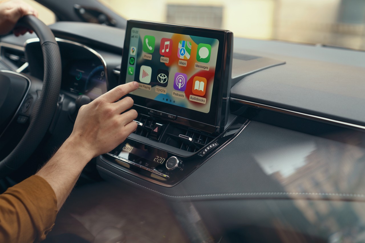 Osoba sedící v Toyotě používá dotykovou obrazovku palubních multimédií. Na displeji se zobrazuje domovská obrazovka Apple CarPlay.